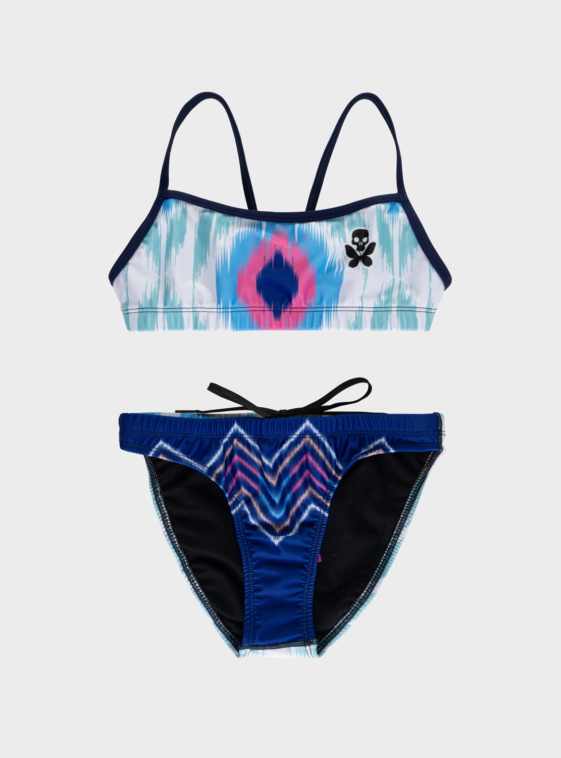 A two-piece bikini set laid flat on a light gray background. The top has a tie-dye pattern in blue, pink, and white with dark navy straps and trim, featuring a central pink and blue diamond motif and a small black skull-and-butterfly logo on the right side.